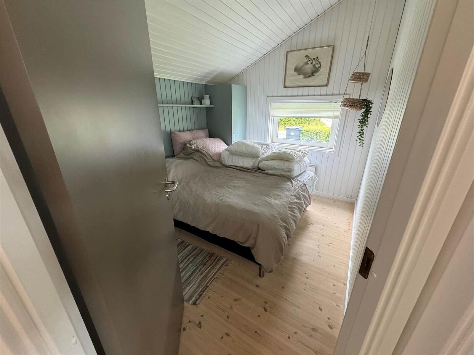 Bedroom with bed, window, and wooden floor. Walls with vertical panels.