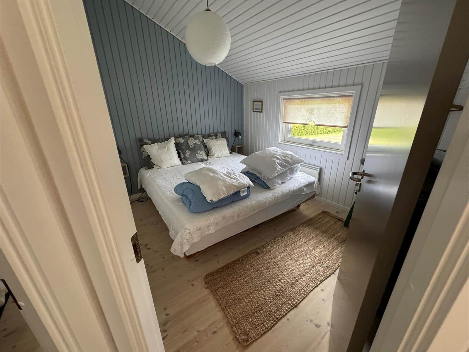 Bedroom with bed, window, and wooden floor. Ceiling and walls are paneled.