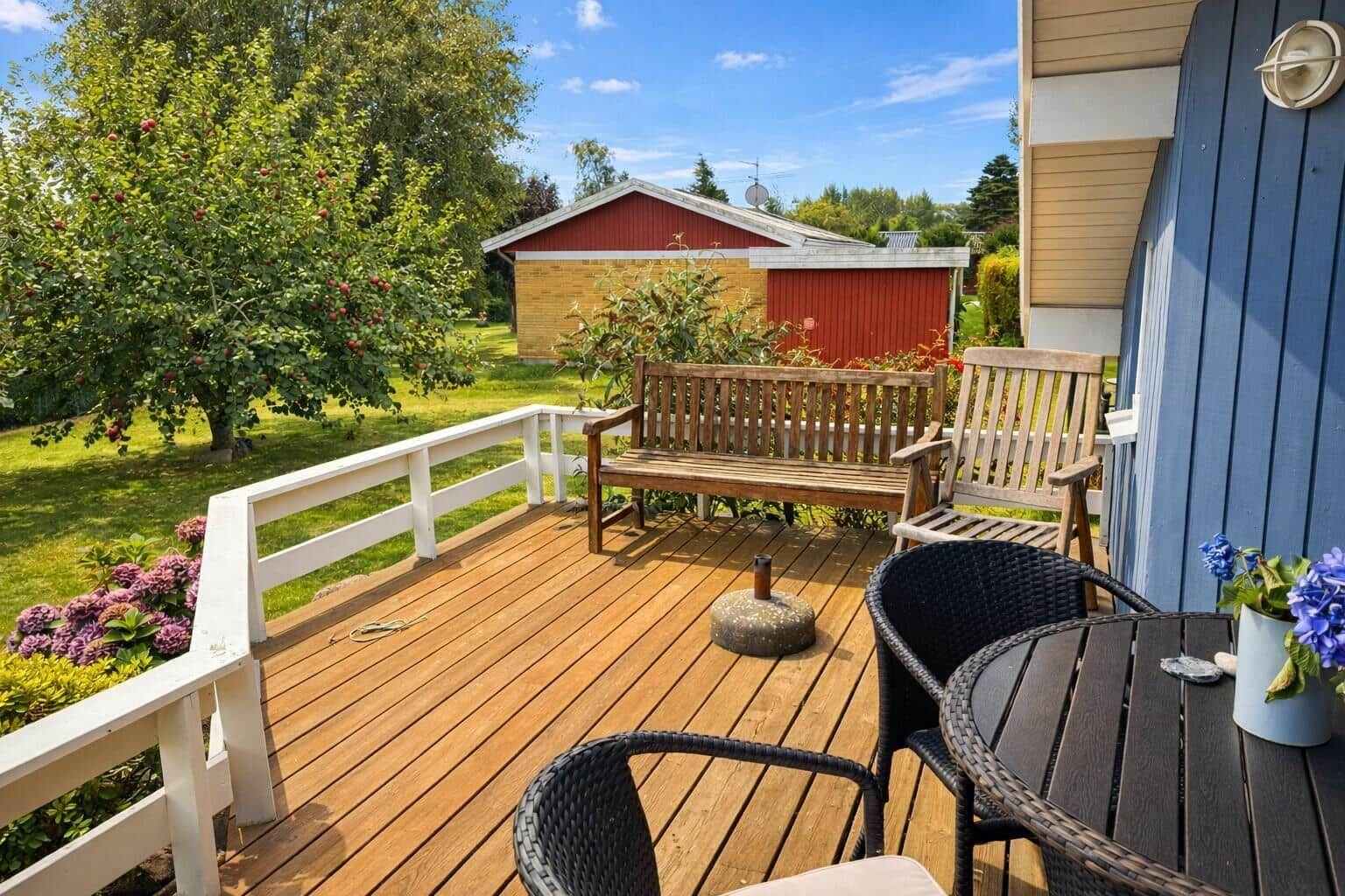 Deck with wooden flooring, garden furniture, and view of an apple tree and a red shed.