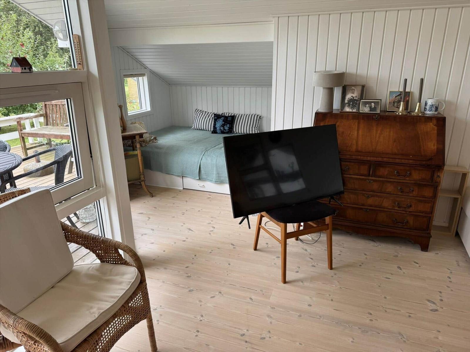 Bedroom with bed, TV, and wooden floor. View of terrace through window.