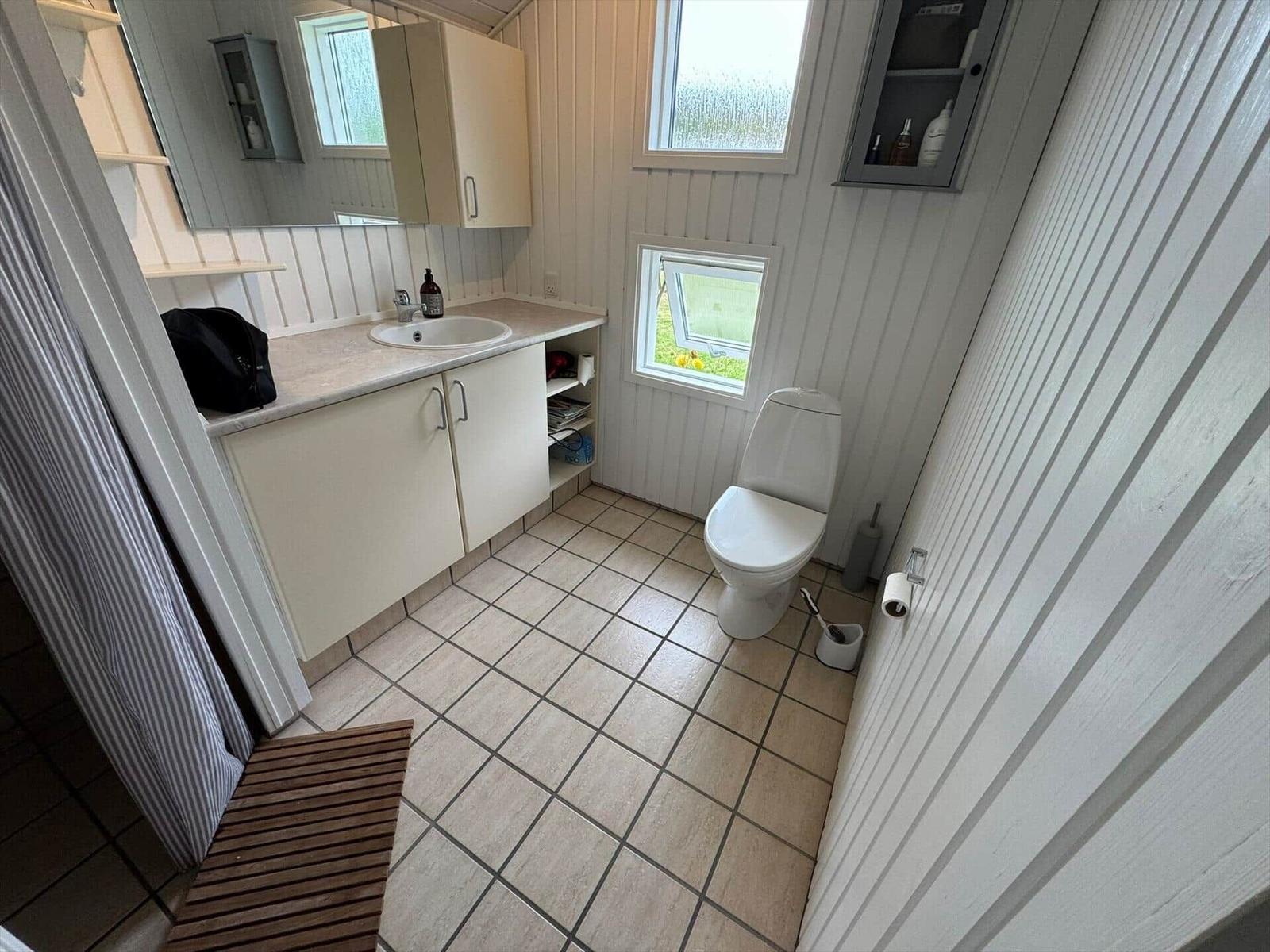 Bathroom with sink, toilet, and shower. White walls and tiles.