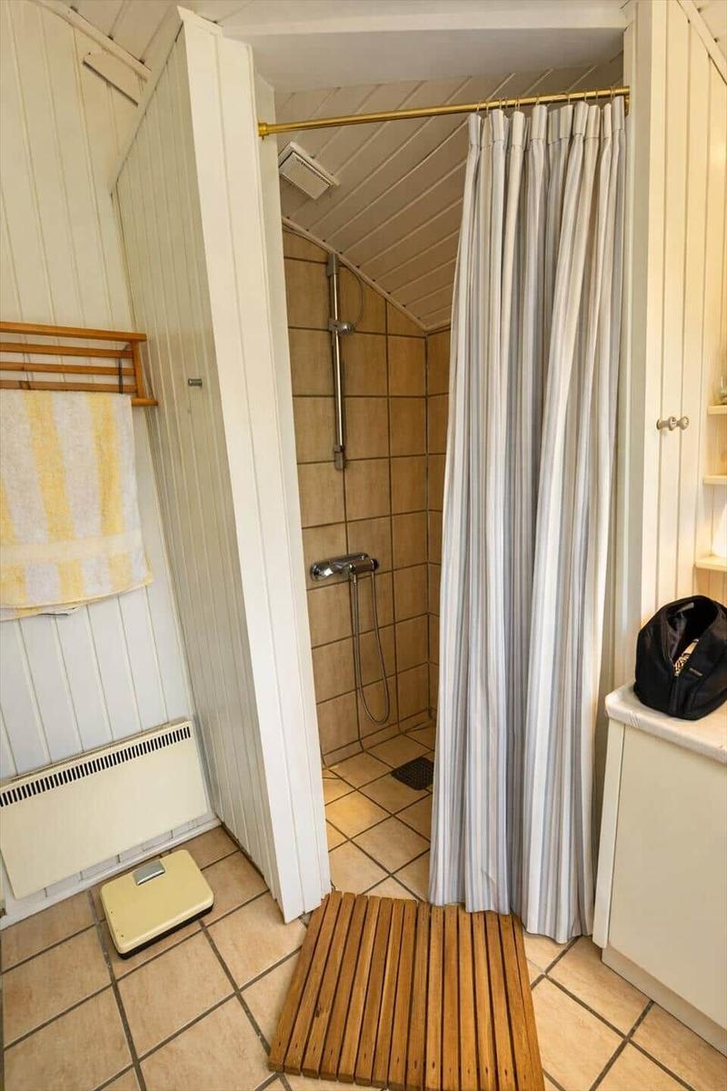 Shower cabin with curtain, shower head, and tiled floor.