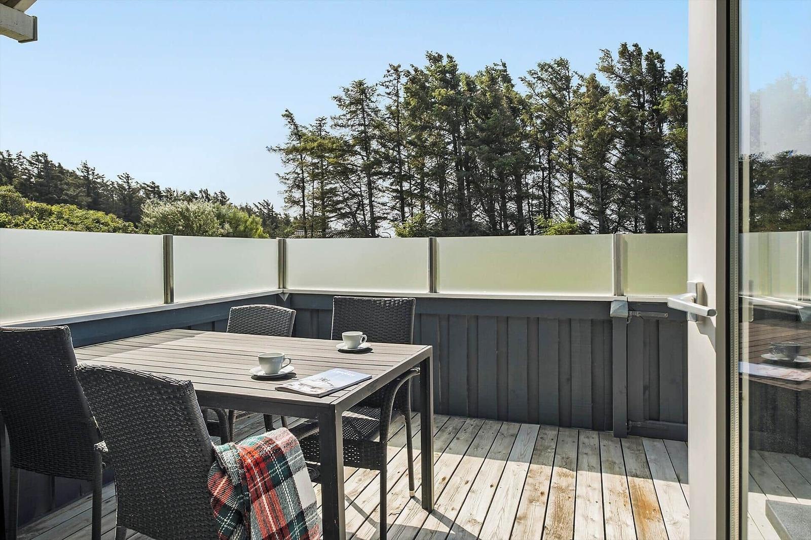 Terrasse mit Tisch und Stühlen, Blick auf Bäume und Himmel.