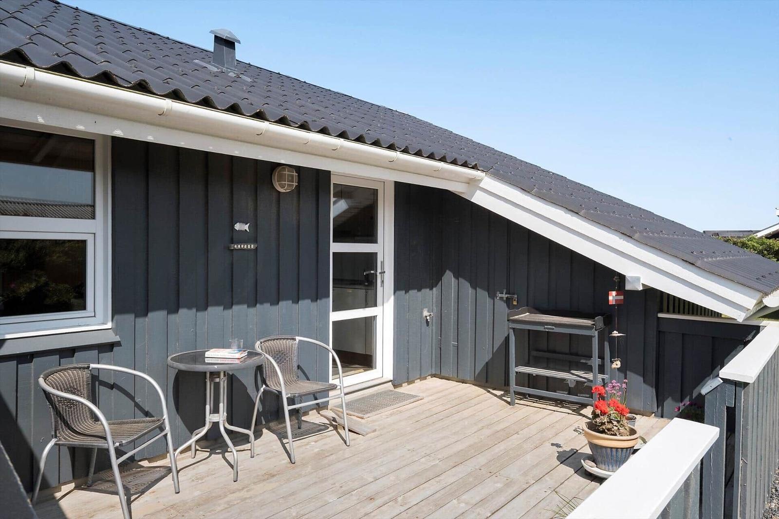 Terrasse mit Tisch, zwei Stühlen und Pflanzen vor einem Haus mit dunkler Fassade.