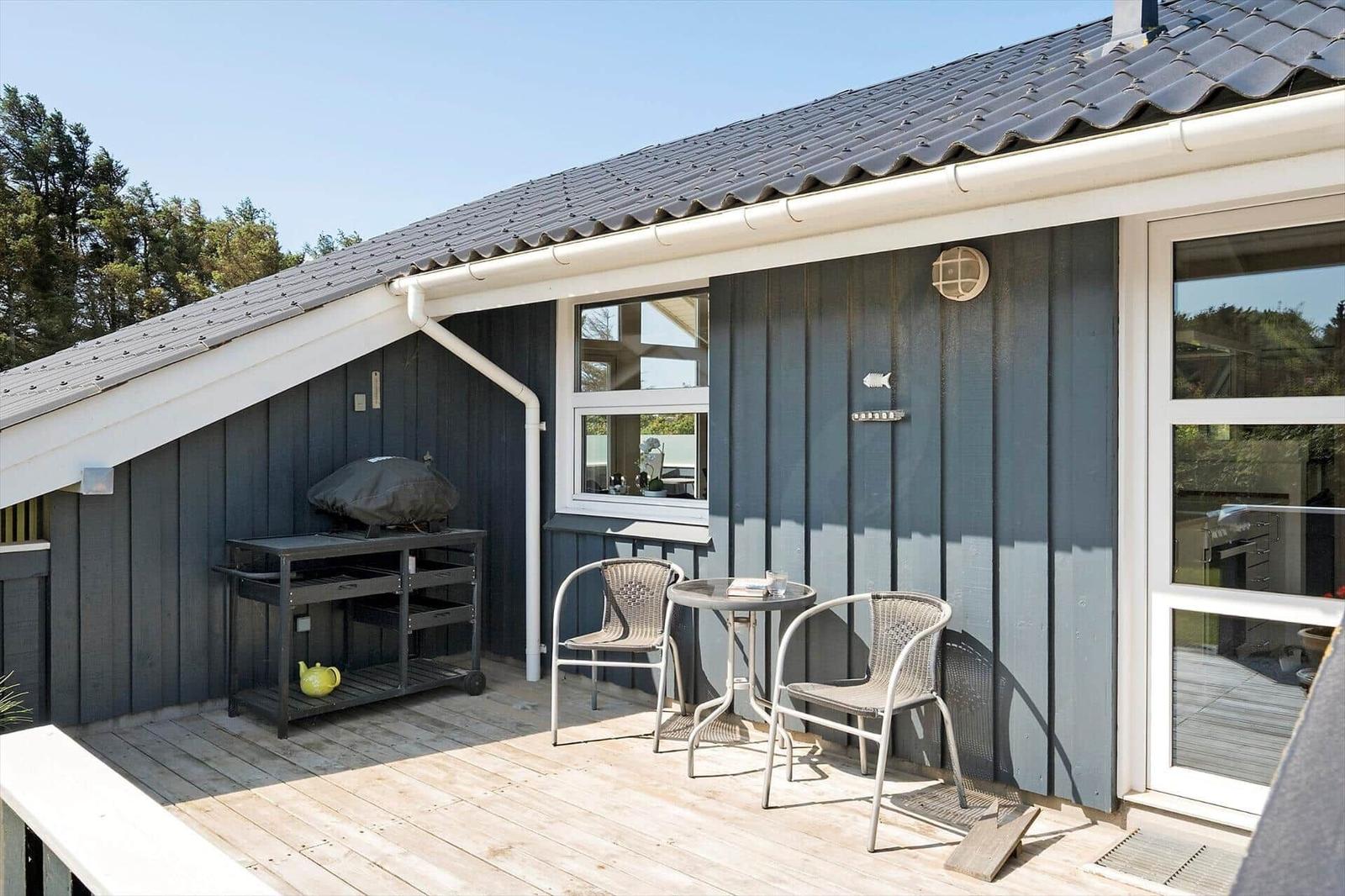 Terrasse mit Tisch, zwei Stühlen und Grill. Holzdecke, graue Wand und Fenster.