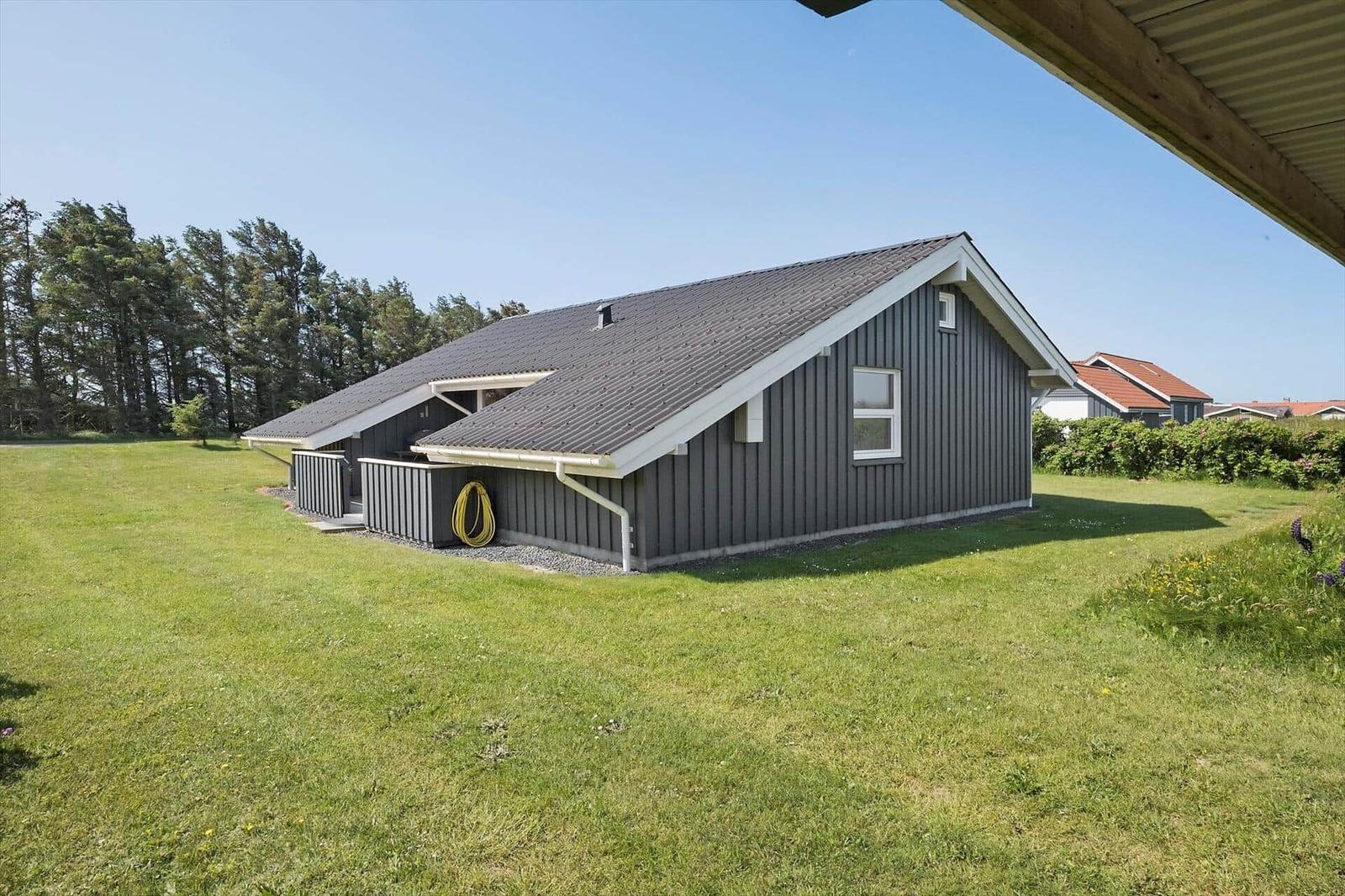 Ein graues Haus mit grünem Rasen und Bäumen im Hintergrund.