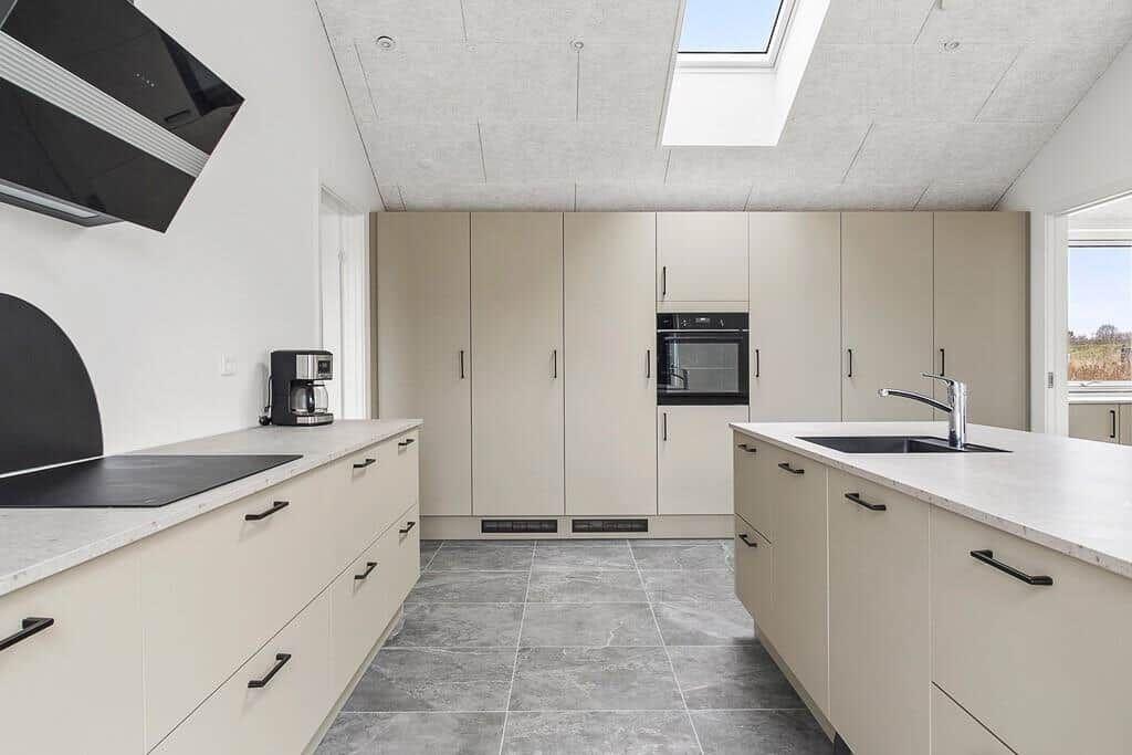 Moderne Küche mit hellen Schränken, Steinplatten und Dachfenster.