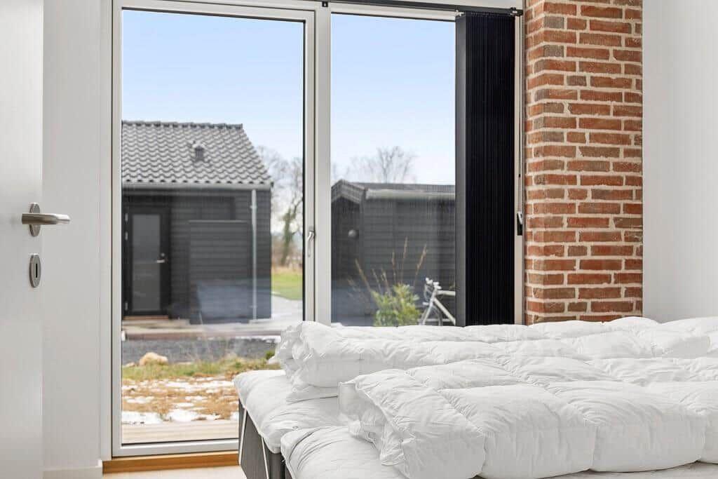 Schlafzimmer mit weißem Bett und großem Fenster zur Außenterrasse.