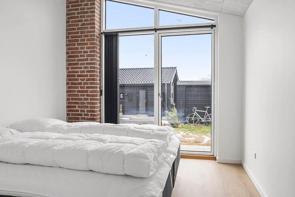 Schlafzimmer mit weißem Bett und großem Fenster zur Außenterrasse.