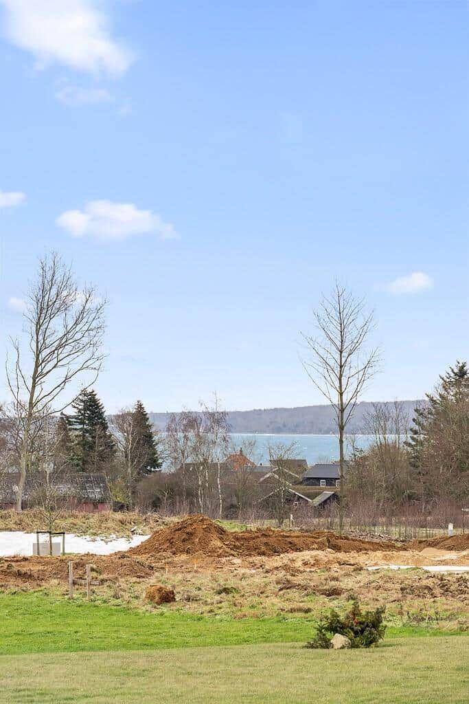 Grünes Feld mit Erdhügeln, Bäumen und Blick auf See und Berge.