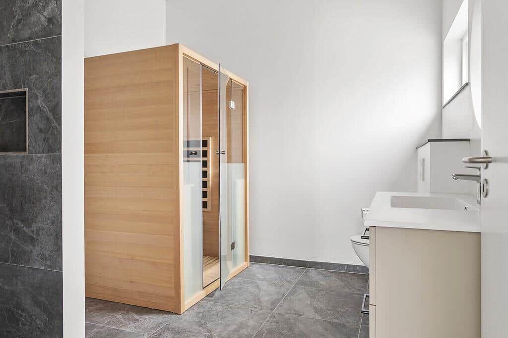 Bad mit Holzsauna, Waschbecken und Toilette. Graue Fliesen und weiße Wände.