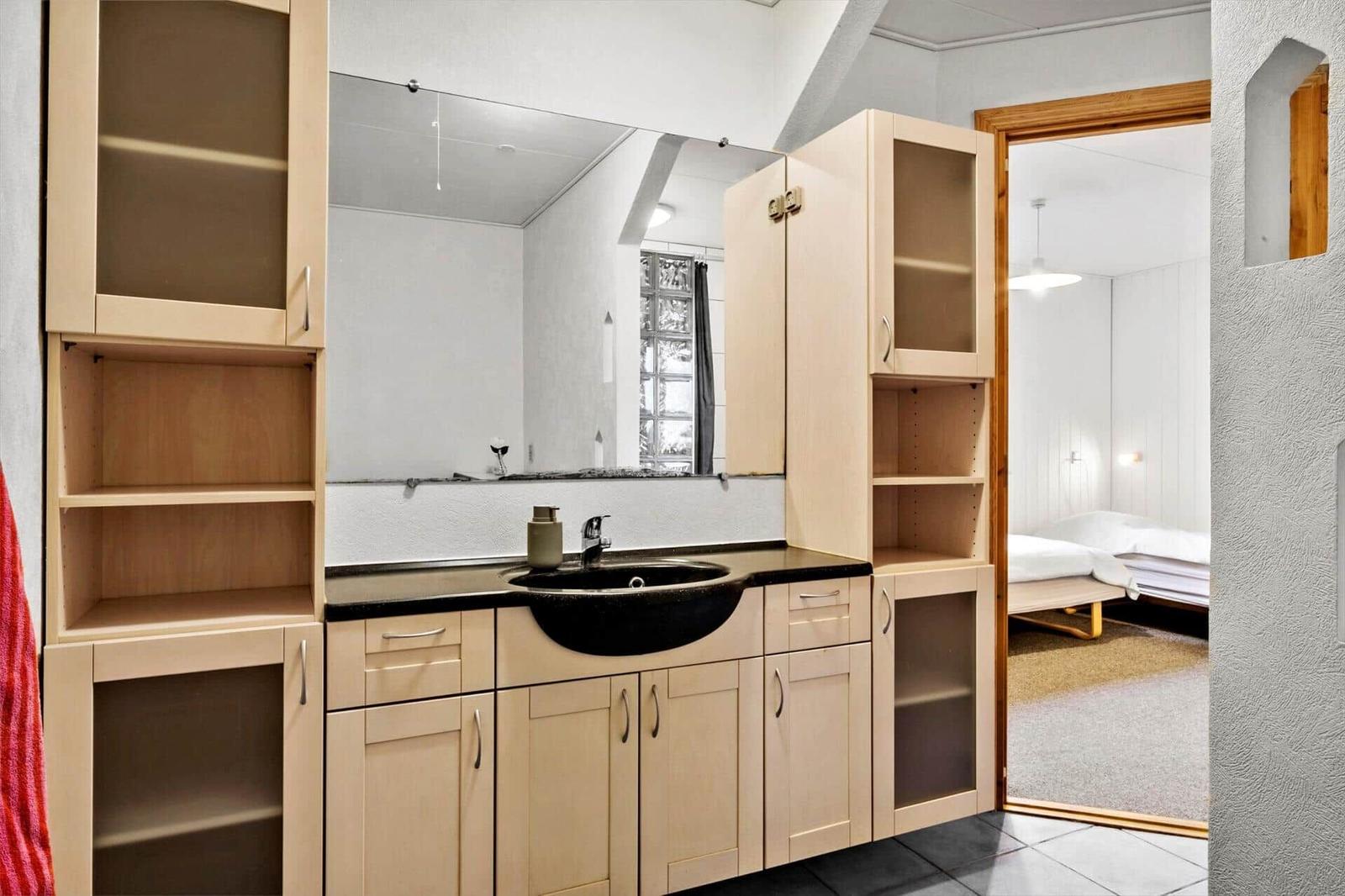 Bathroom with sink, mirror, and wooden cabinets. Corridor to the bedroom.