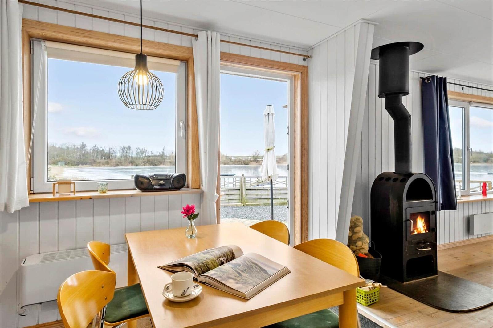 Dining room with wooden table, chairs, and wood stove. View of water and terrace.