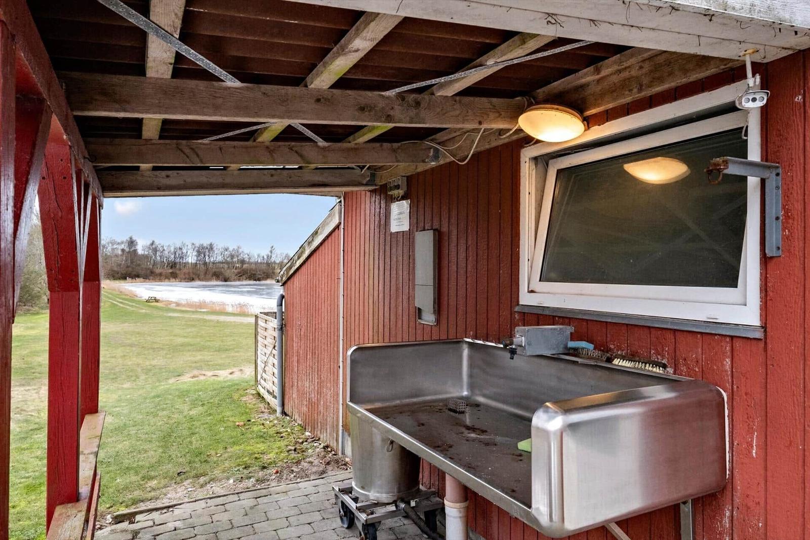 Outdoor sink at red wooden hut with view of pond and grass.