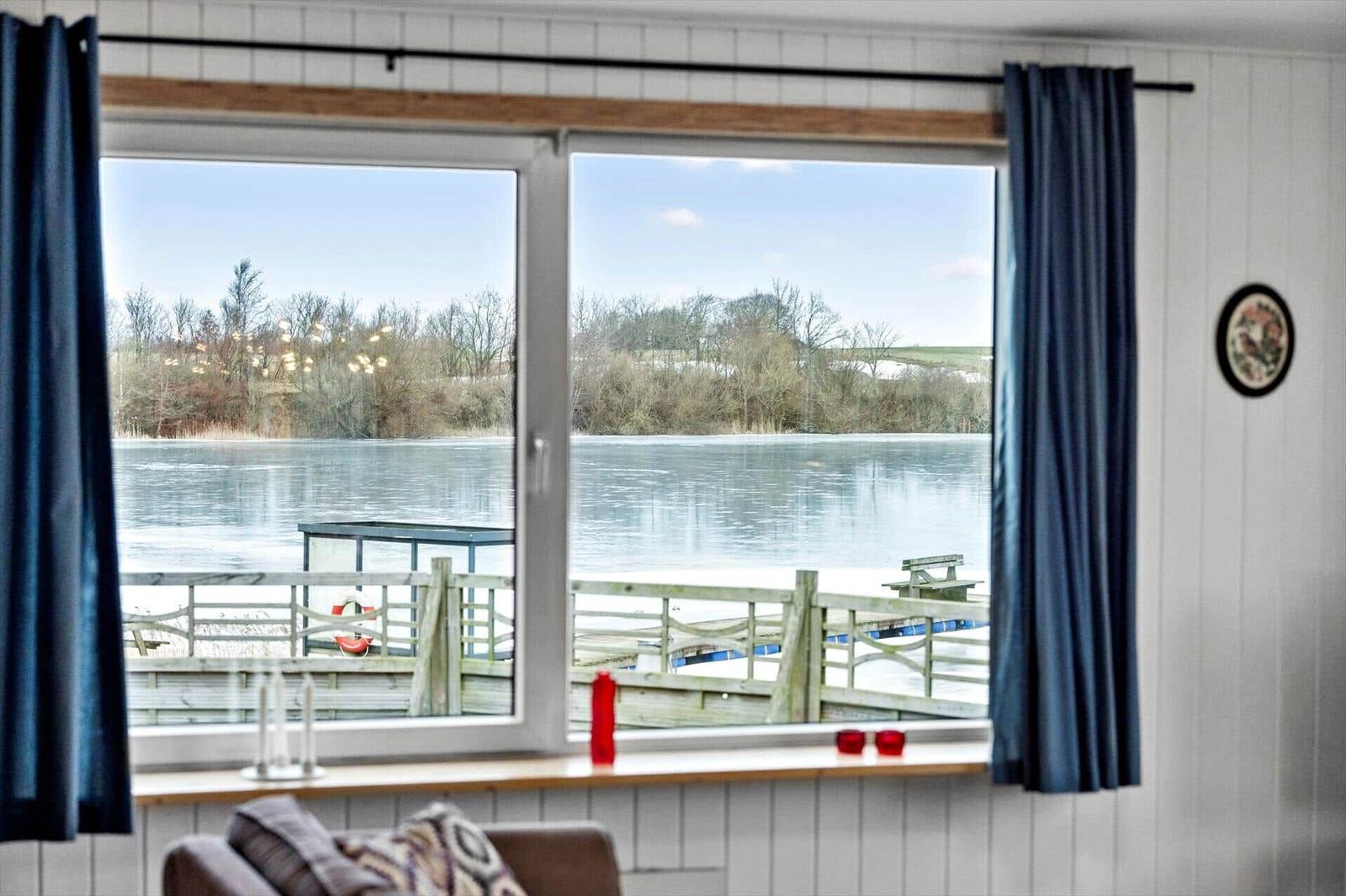 Through the window, a frozen lake with a wooden bridge and trees is visible.