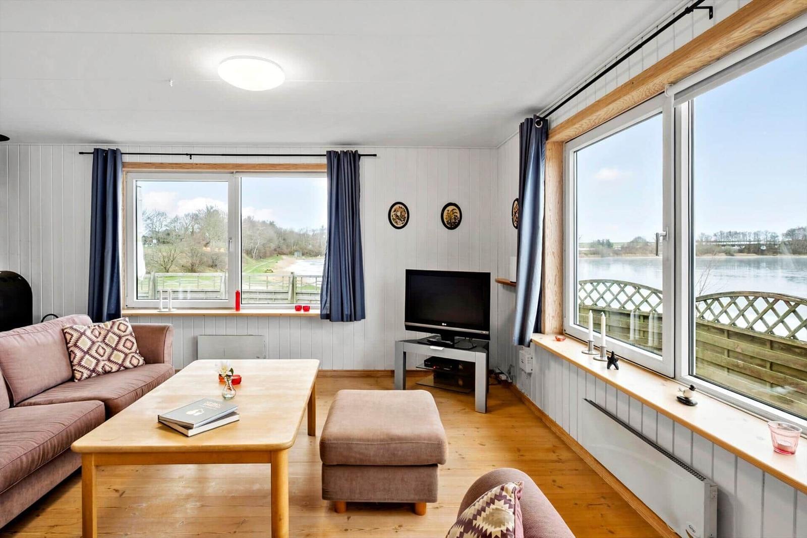 Living room with sofa, coffee table, and TV. Large windows with water view.