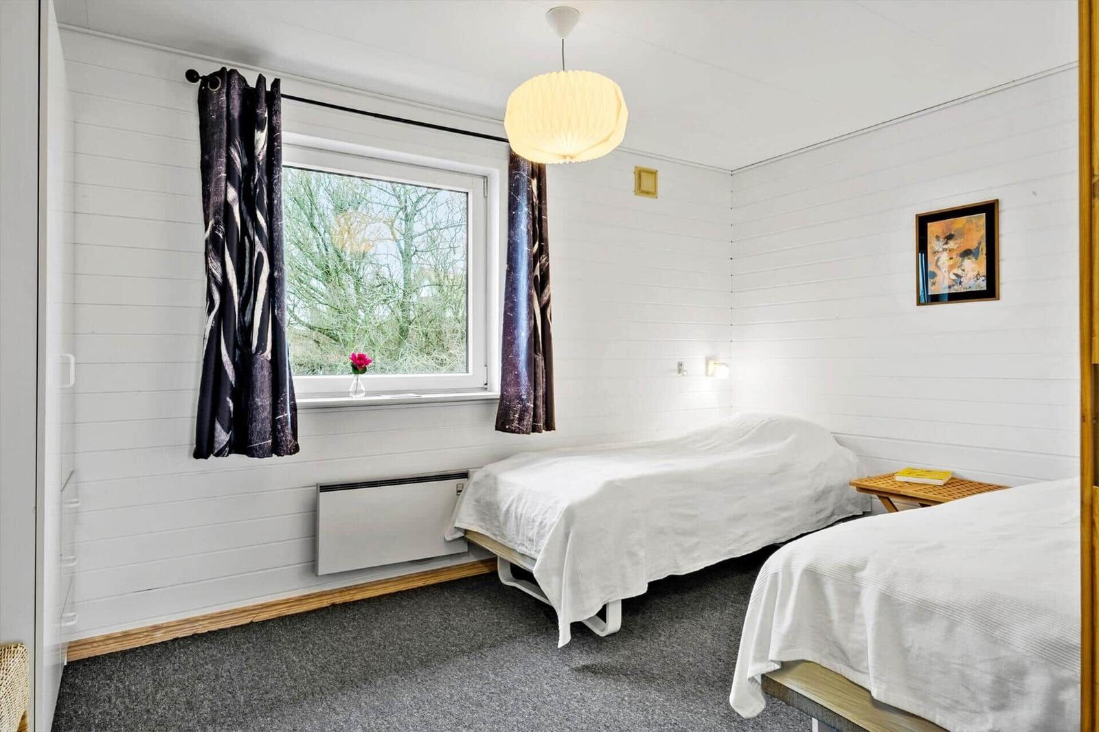 Two beds, window with curtains, pendant light, and wall art.