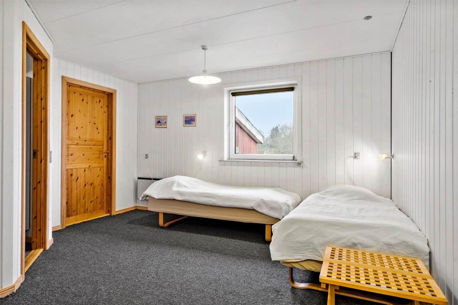 Two beds, window, wooden doors, and gray carpet in a bedroom.