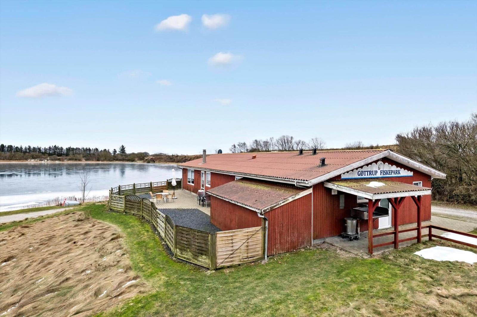 Red building by the lake with grill area and terrace.