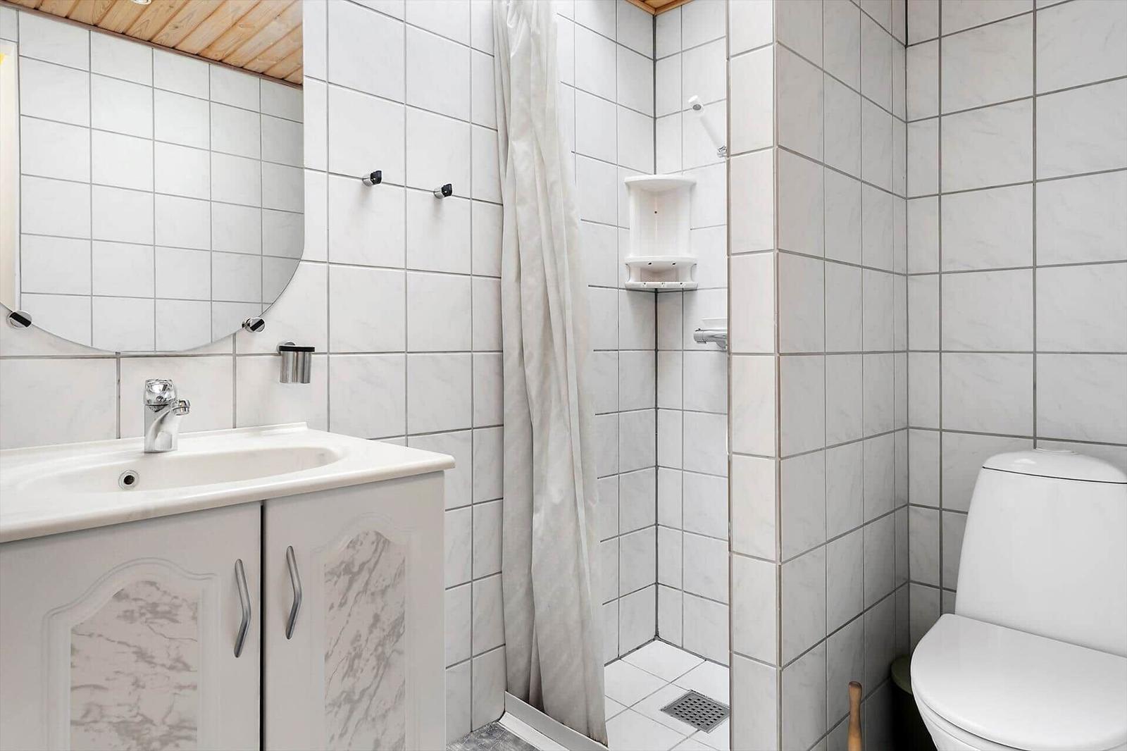 Badezimmer mit Dusche, Waschbecken und Toilette. Fliesenwand und Spiegel.