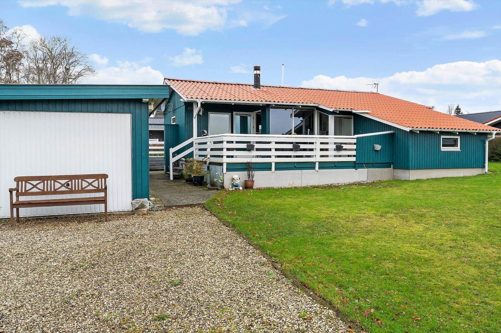 Ein Haus mit Terrasse, grünem Garten und Holzbank vor Garage.