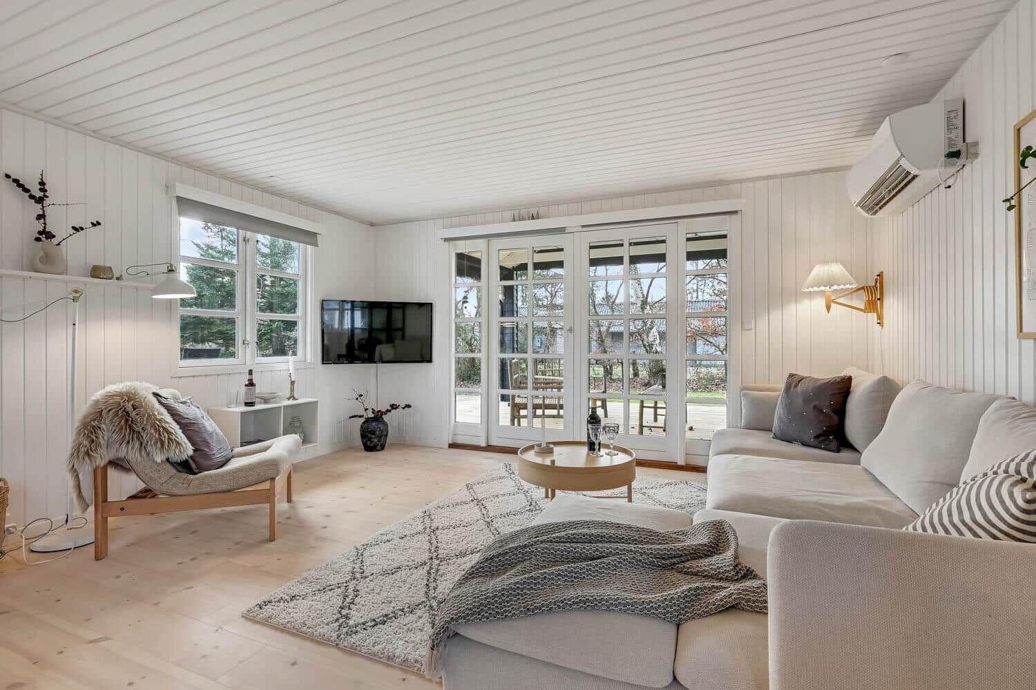 Wohnzimmer mit Sofa, Sessel, TV und Glastüren zum Garten.