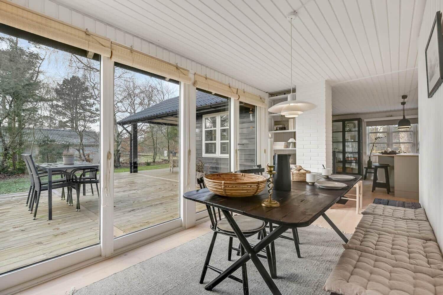 Essbereich mit Tisch, Stühlen und Sitzbank. Große Fenster zeigen Terrasse und Garten.