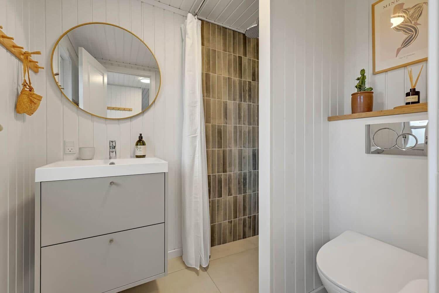 Badezimmer mit Waschbecken, Dusche und Toilette. Holzvertäfelung und Spiegel.
