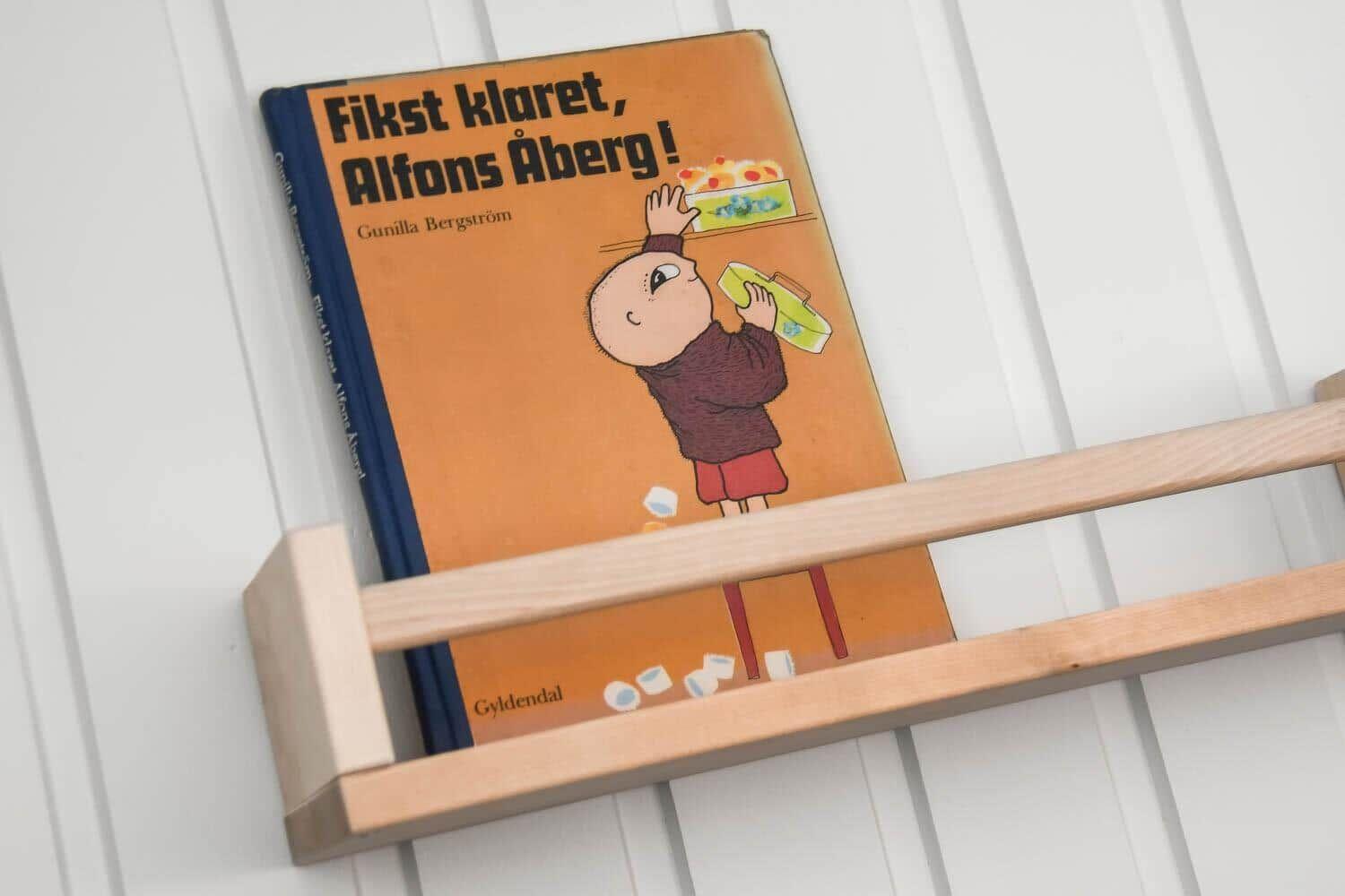 Ein Buch liegt auf einem Holzregal an einer weißen Wand.