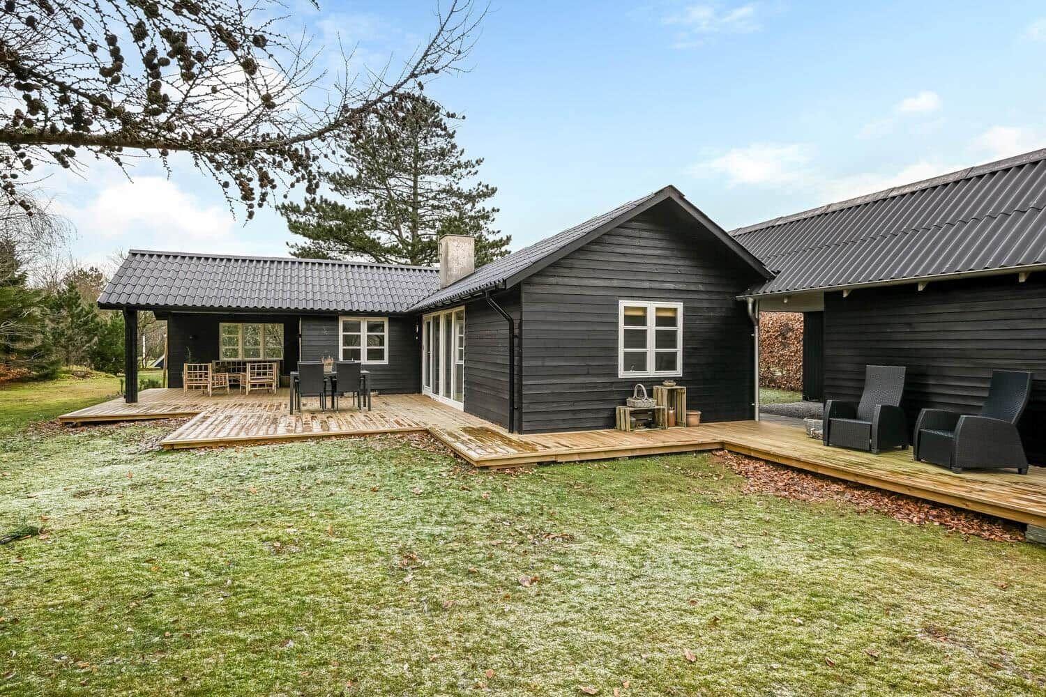 Schwarzes Holzhaus mit Terrasse und Garten. Außentische und -stühle sind vorhanden.
