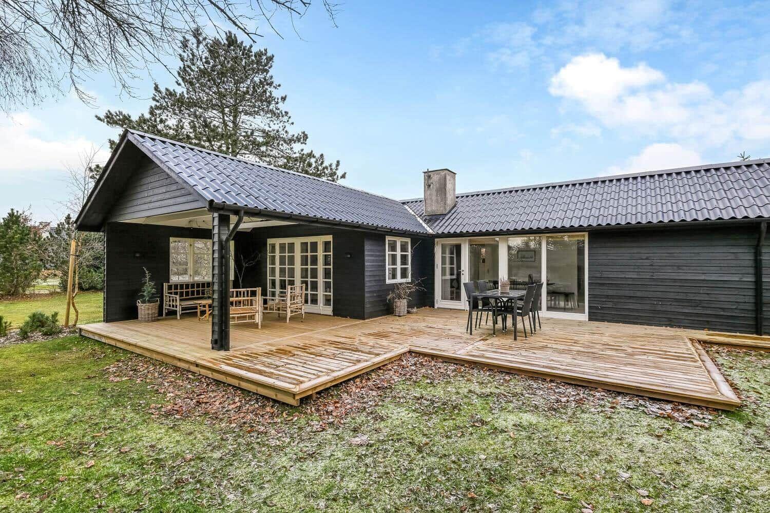 Schwarzes Holzhaus mit großem Balkon und Garten. Terrasse mit Sitzgelegenheiten.