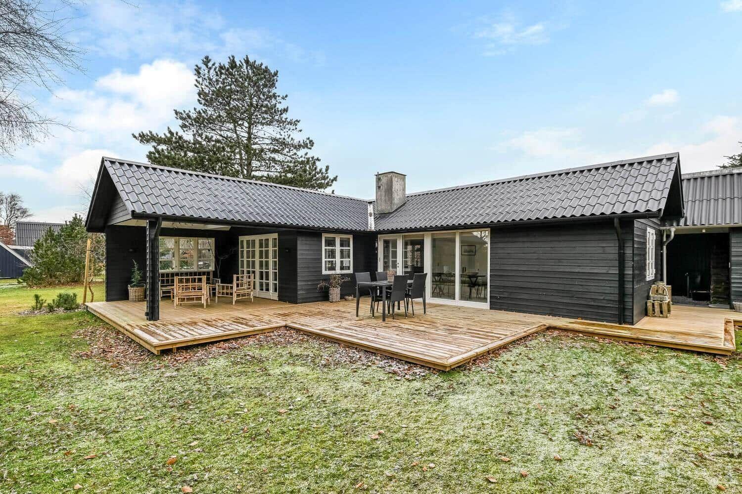 Moderne Holzhütte mit Terrasse und Garten. Grosse Fenster und Sitzgelegenheiten.