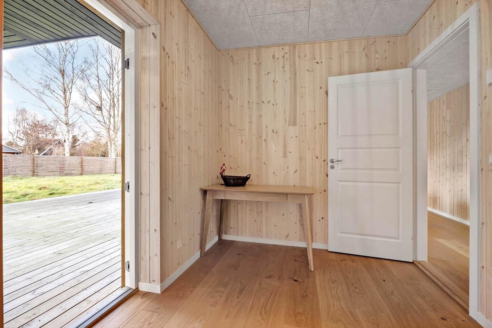 Eingangsbereich mit Holzwand, Tisch und Tür. Durchgang zur Terrasse.