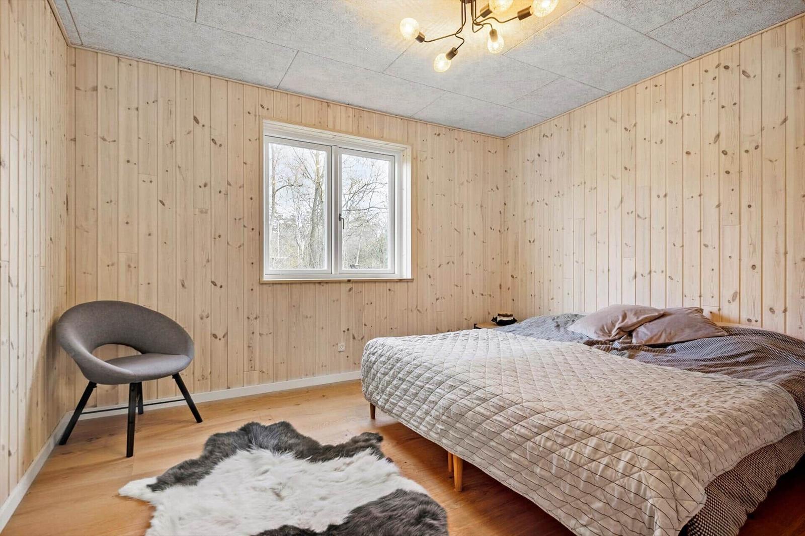 Schlafzimmer mit Holzwand, Bett, Stuhl und Fenster.