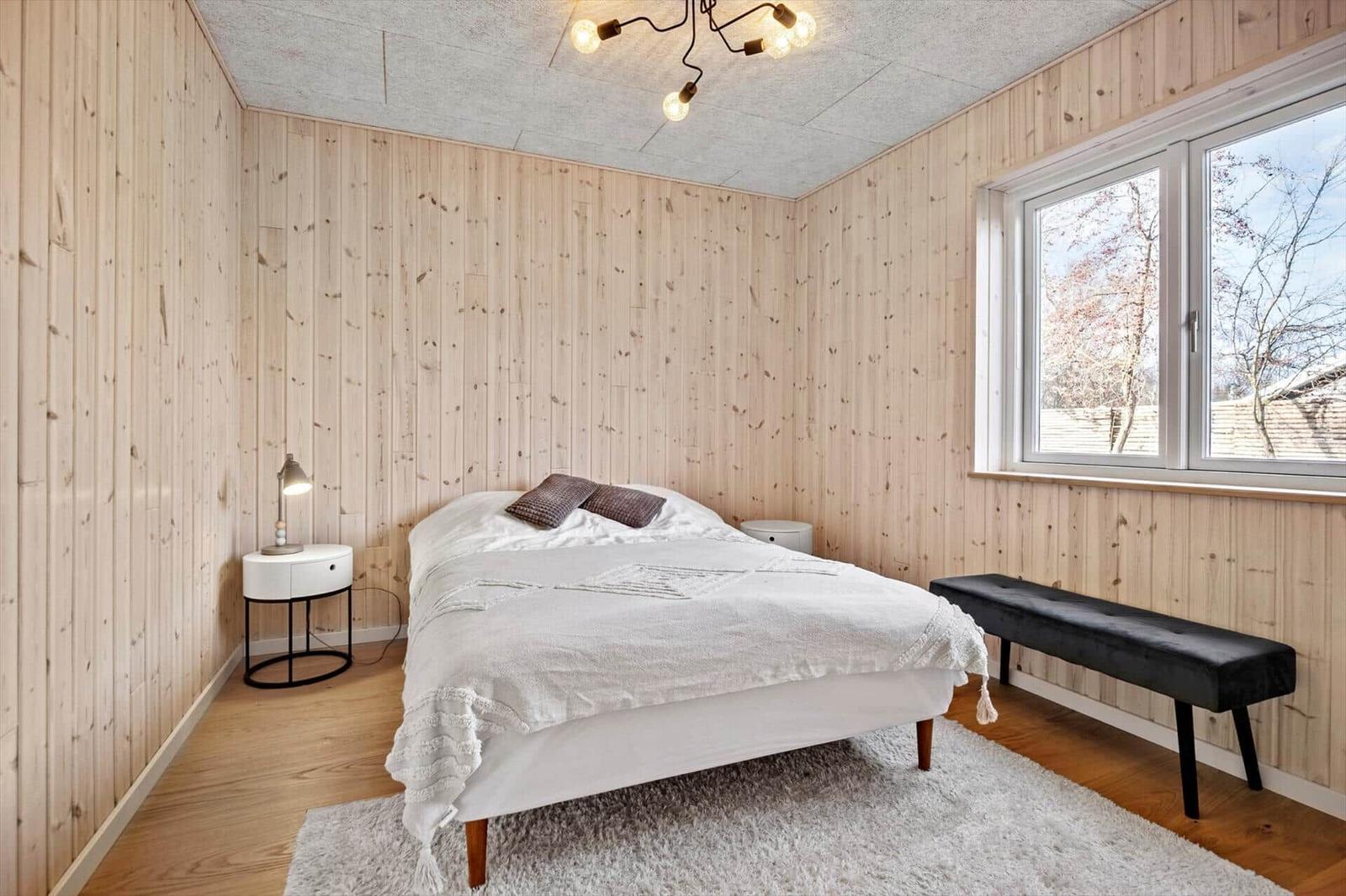 Schlafzimmer mit Holzwand, Bett, Fenster und Bank.
