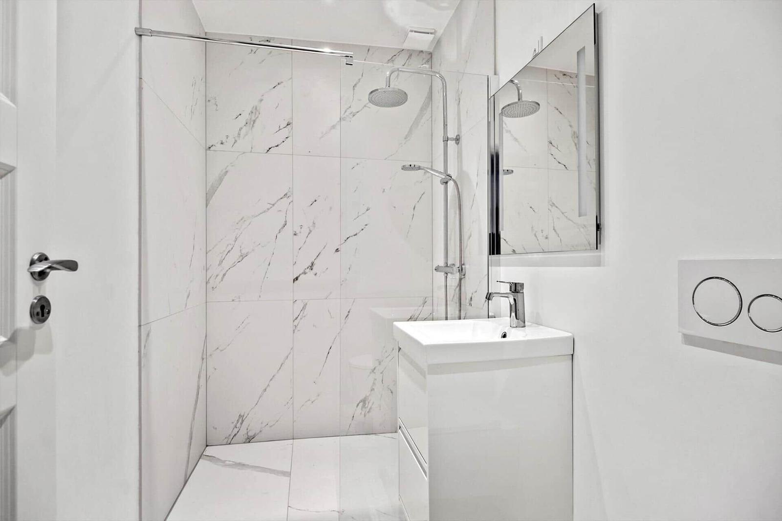 Badezimmer mit Dusche, Waschbecken und Spiegel.