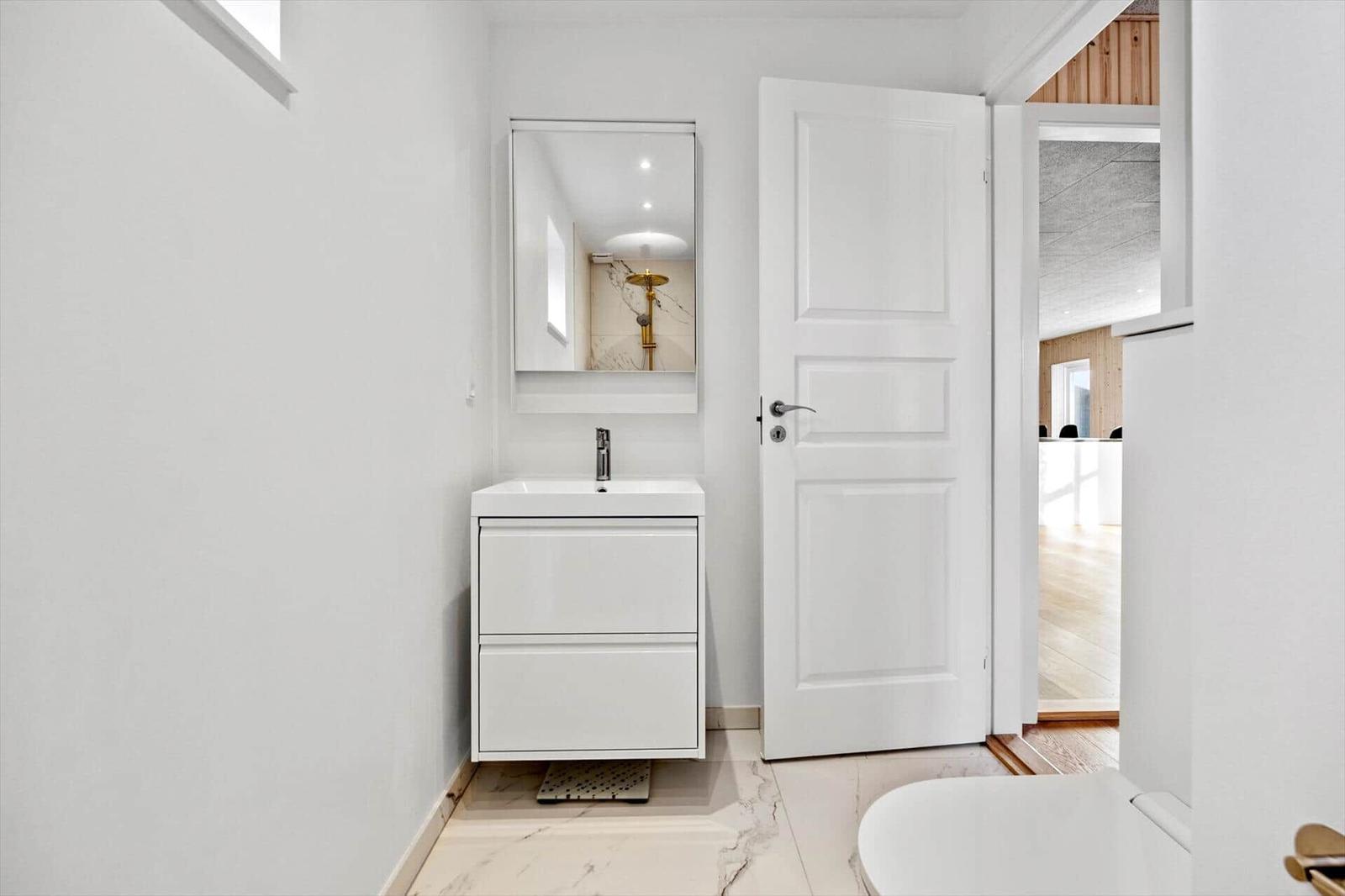 Badezimmer mit Waschbecken, Spiegel und Dusche. Tür führt in Wohnbereich.