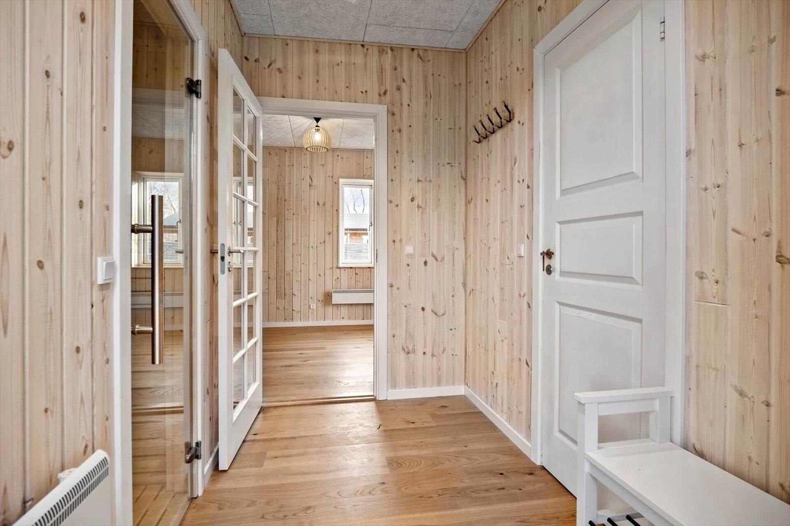 Flur mit Holzwandverkleidung, weißen Türen und Holzboden. An der Wand hängen Haken.