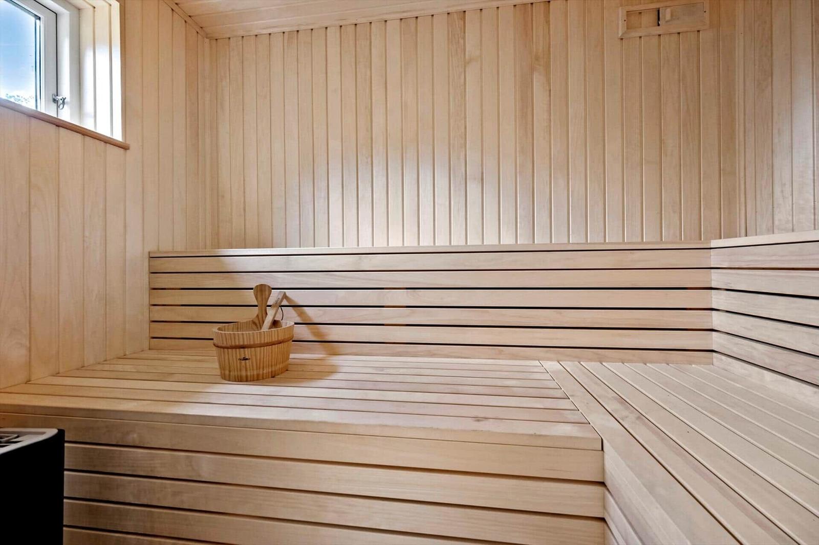 Sauna mit Holzbank und Eimer. Fenster und Holzwände sichtbar.
