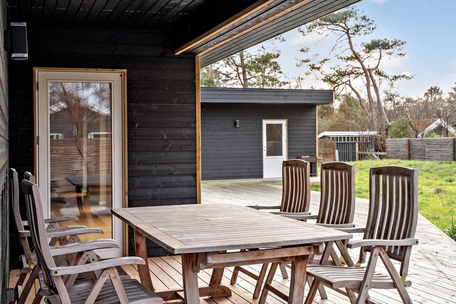 Terrasse mit Holztisch und Stühlen, Blick auf Garten und Nebengebäude.