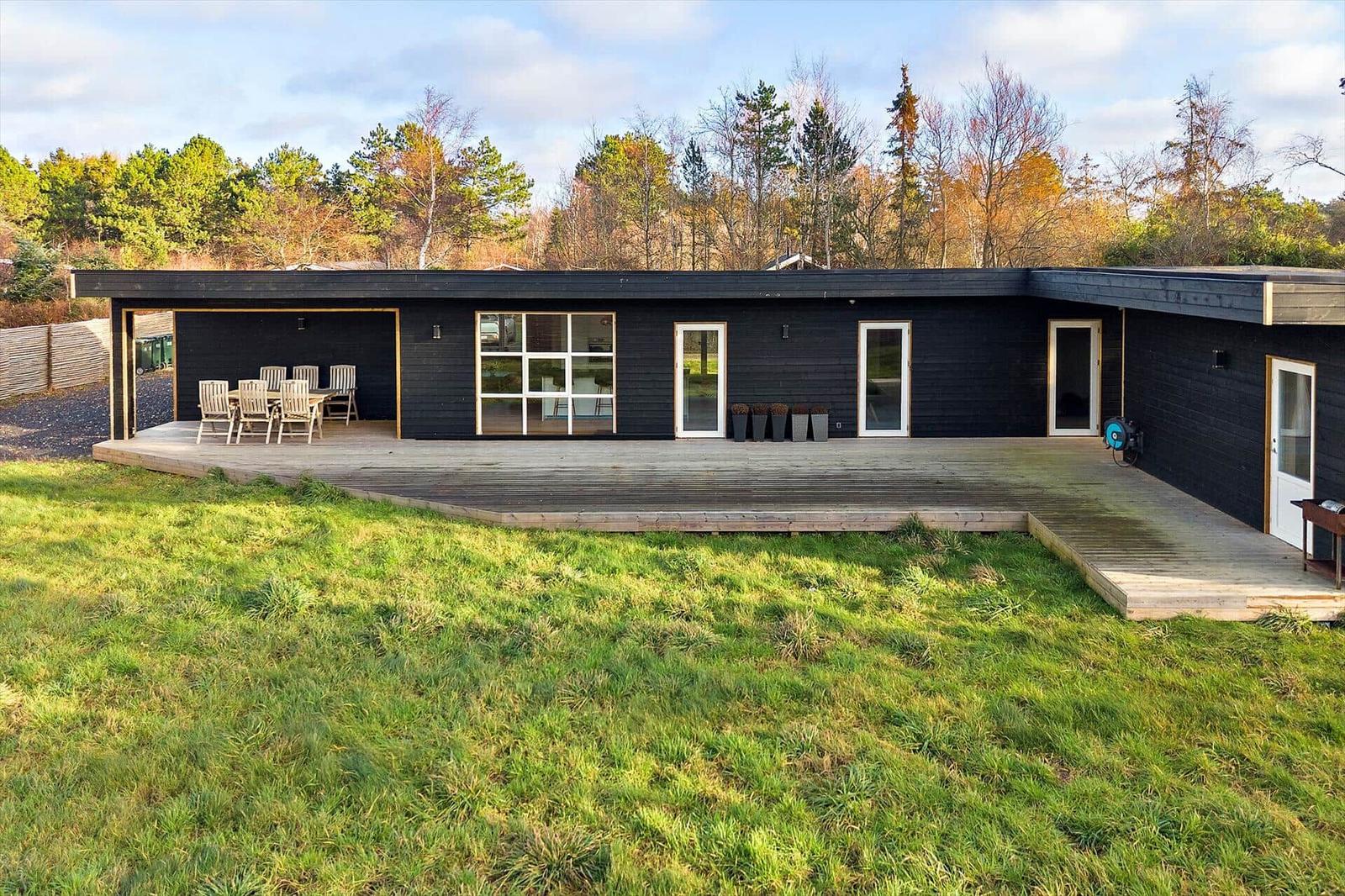 Moderne schwarze Hütte mit Terrasse und Garten. Sichtbar: Tisch, Stühle, Fenster, Türen.