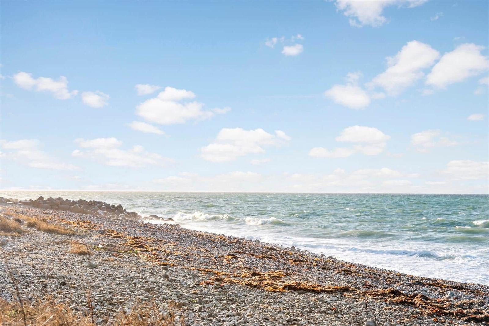 Steiniger Strand mit Wellen und blauem Himmel mit weißen Wolken.