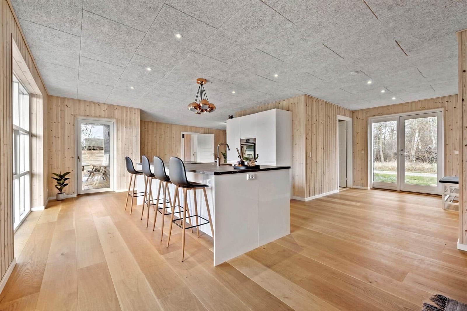 Moderne Küche mit Insel und Barhocker. Holzwände und Boden. Glastüren zu Außenbereich.