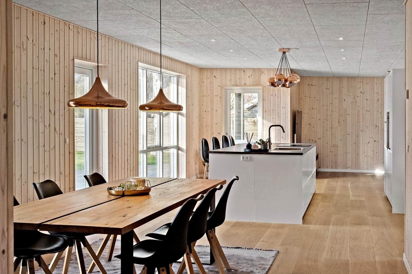 Essbereich mit Holztisch und schwarzen Stühlen. Küche mit weißem Küchenblock und Holzwänden.
