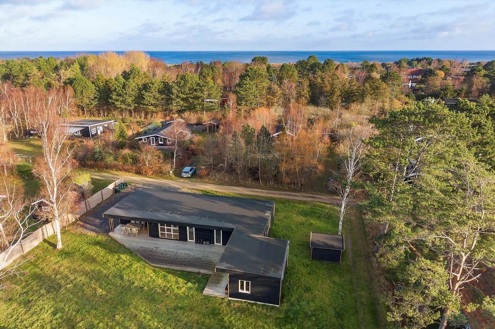 Modernes Haus mit Terrasse, umgeben von Wald und Blick auf Meer.