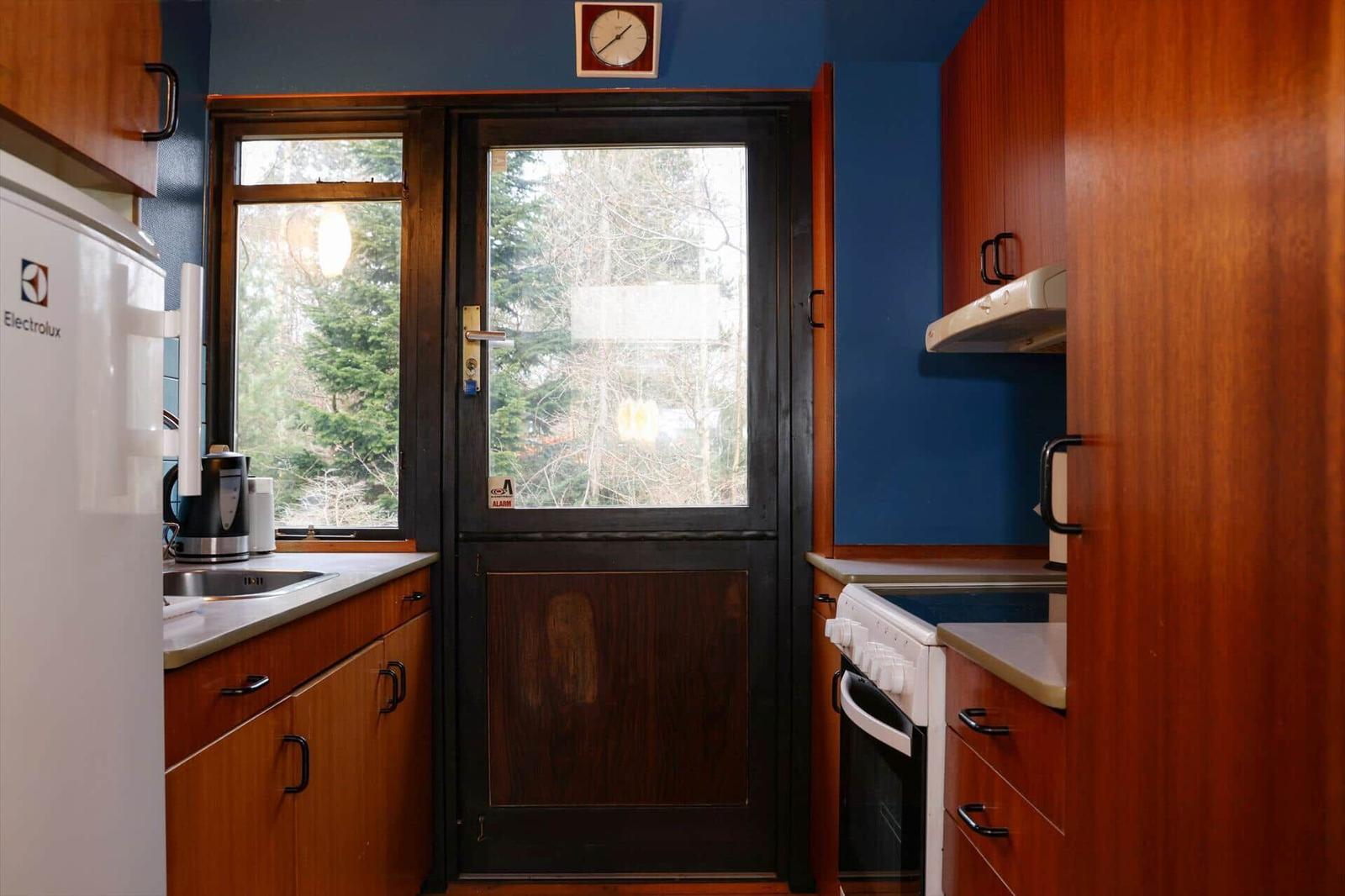 Kitchen with wooden cabinets, refrigerator, and door to outside area.