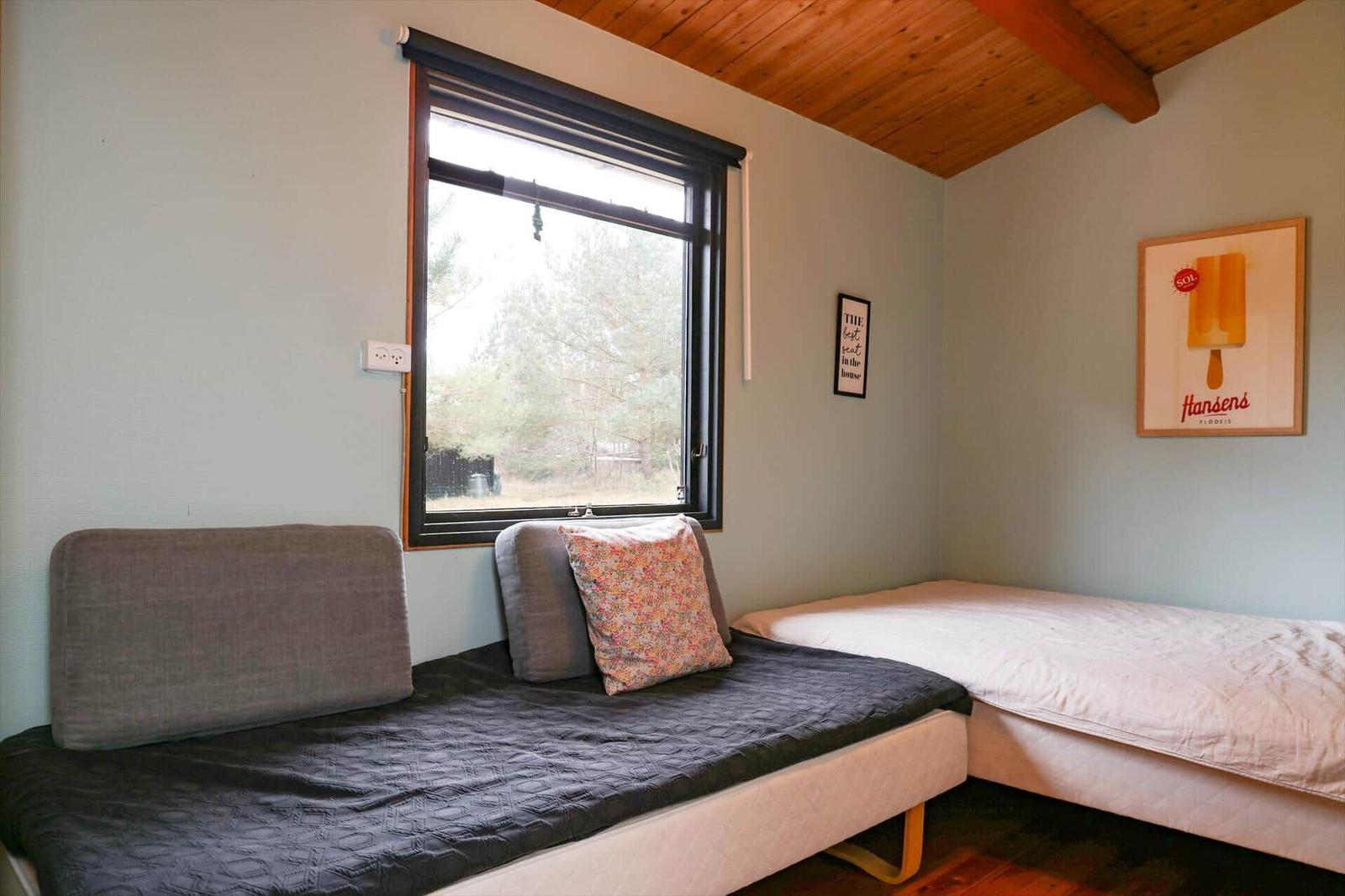 A bedroom with two beds, a window, and a wooden ceiling.