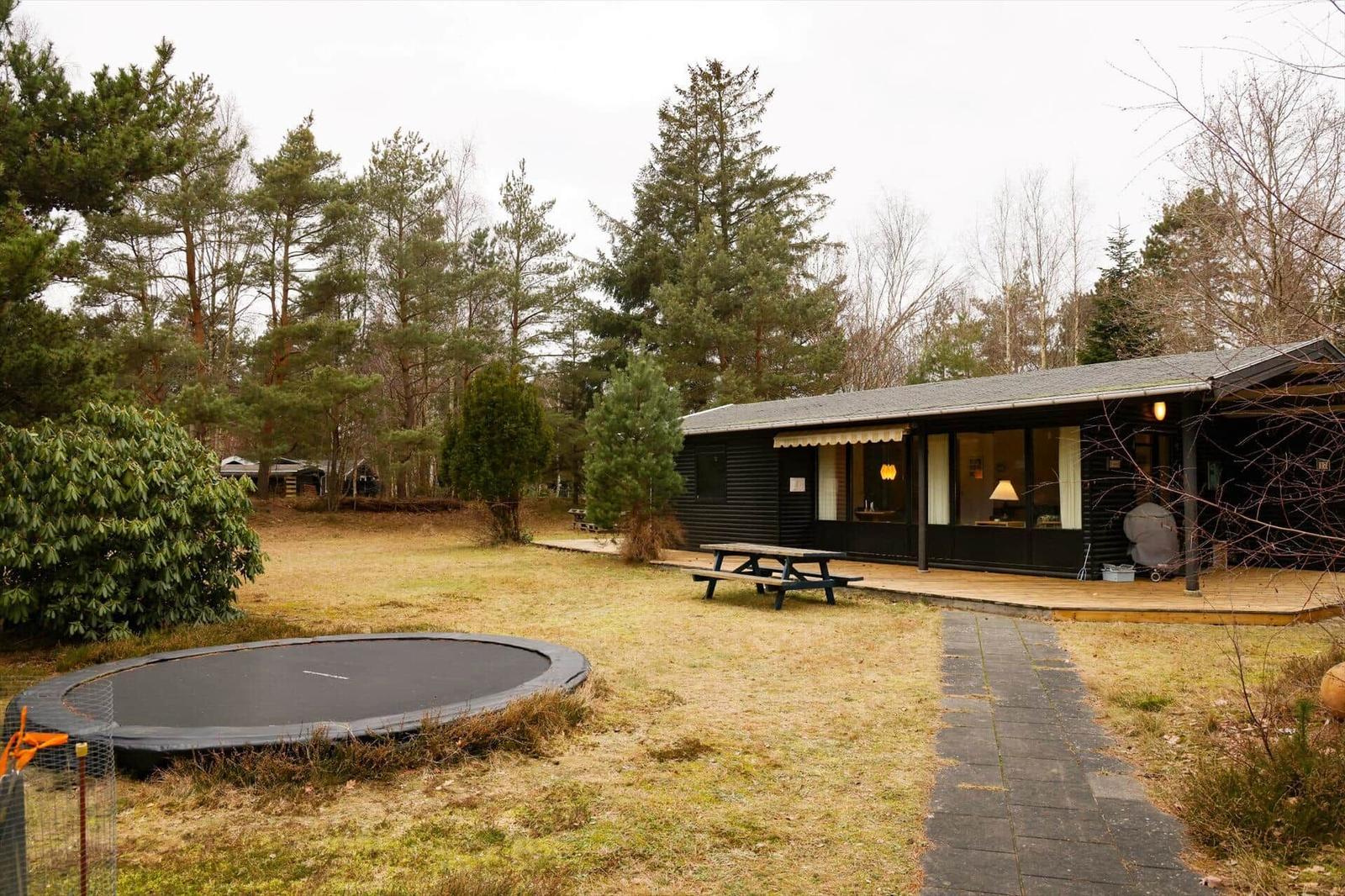 A modern wooden house with a terrace, picnic table, and trampoline in the woods.
