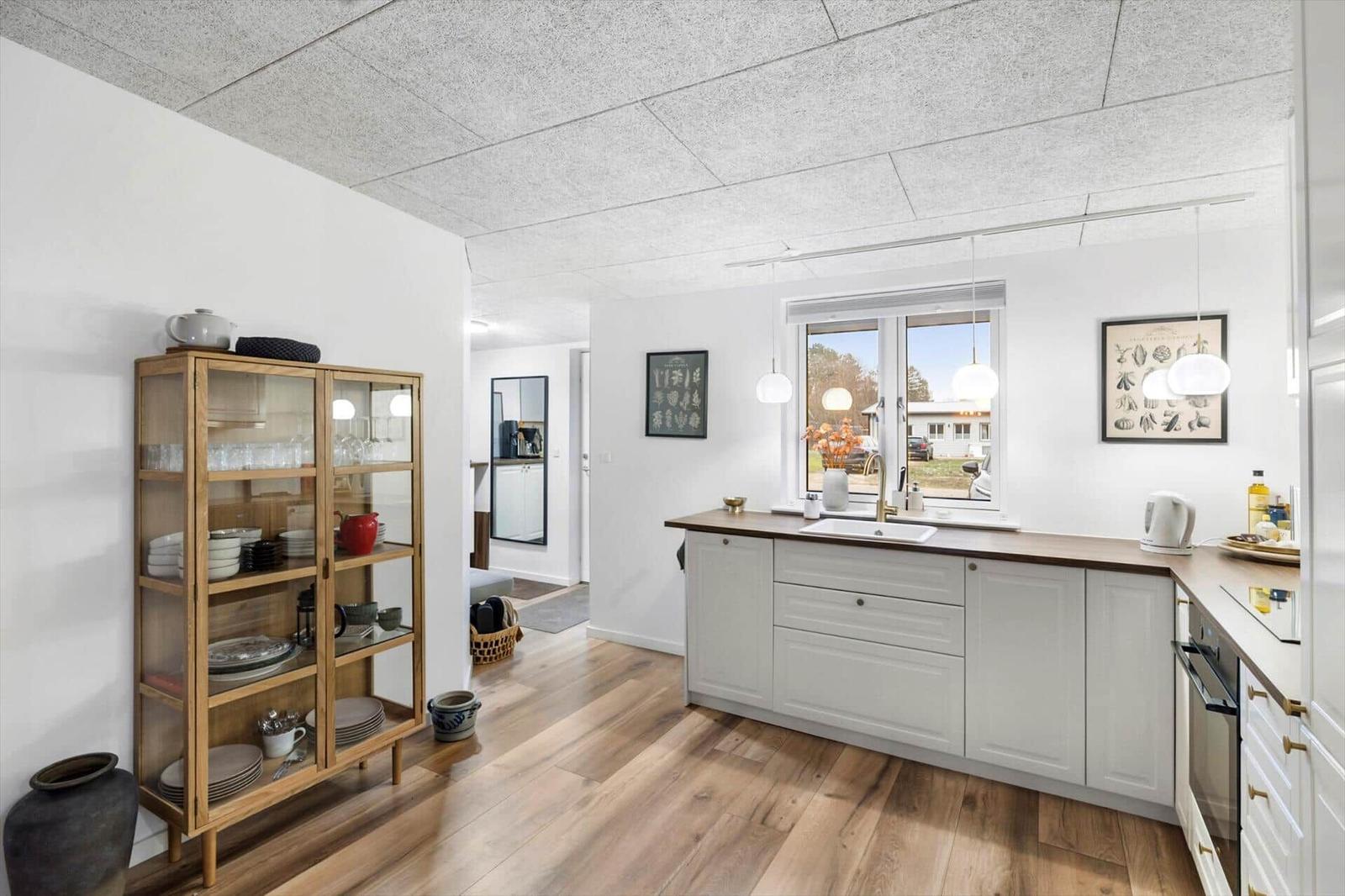 Kitchen with wooden floor, white cabinets, and glass cabinet. Window with view outside.