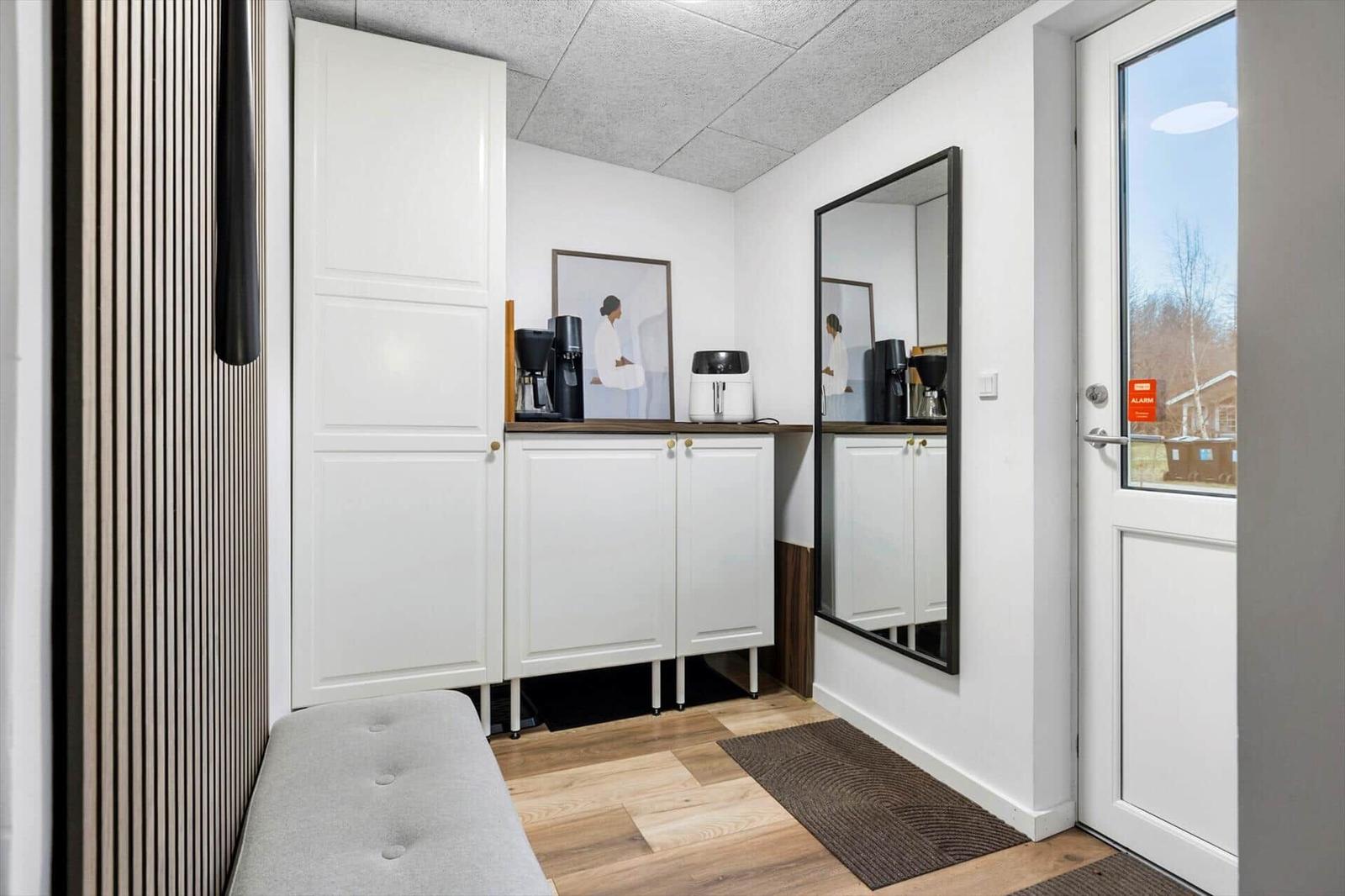 Entryway with mirror cabinet, coffee machine, and wooden floor.